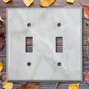 May include: A white light switch cover with a marble pattern and two toggle switches.