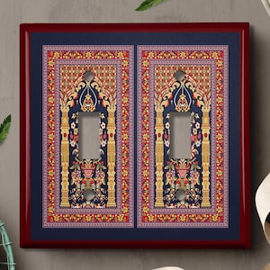 May include: A pair of light switch covers with a decorative design featuring a red, gold, and blue patterned rug with an ornate archway. The switch covers are framed in a dark red wood.