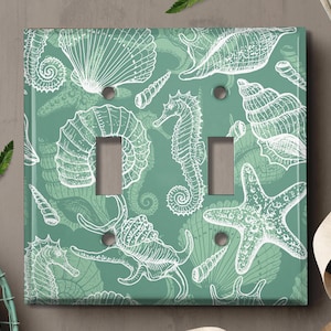May include: A light green light switch cover with a white seashell and seahorse pattern.