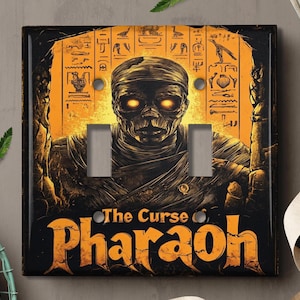 May include: A light switch cover with a graphic of a mummy with glowing eyes. The text "The Curse of Pharaoh" is printed in orange on a black background.