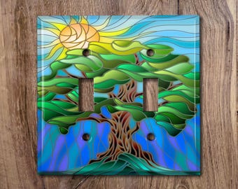 Könnte beinhalten: Ein Lichtschalter-Abdeckung aus Buntglas mit einem stilisierten Baum mit grünen Blättern und einem braunen Stamm. Der Hintergrund ist ein blauer Himmel mit einer gelben Sonne.