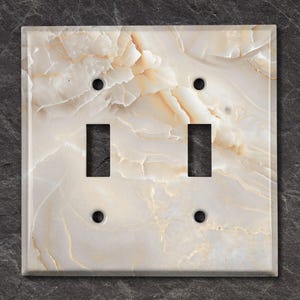 May include: A white double light switch cover with a beige marble pattern.