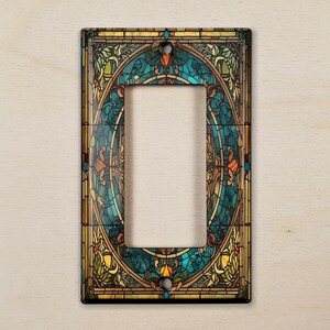 May include: A decorative light switch cover with a stained glass design featuring a circular pattern of blue, green, yellow, and orange colors.