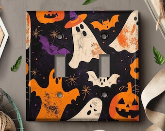 May include: A black light switch cover with a Halloween theme. The design features orange and white ghosts, a purple bat, and a jack-o'-lantern on a black background.