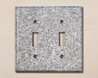 May include: A double light switch cover plate with a gray and white speckled granite pattern.