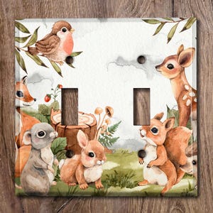 Peut inclure: Une plaque de prise de courant avec un thème animalier de la forêt. Le motif représente un écureuil brun, un lapin blanc, un cerf brun, une souris brune et un oiseau brun avec des accents rouges. L'arrière-plan est un motif aquarelle vert clair et brun.
