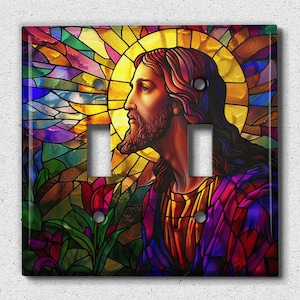 May include: A stained glass light switch cover featuring a colorful image of Jesus Christ with a halo. The background is a vibrant mix of blues, greens, yellows, and reds.