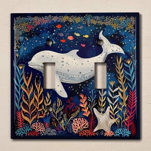 May include: A light switch cover featuring a white dolphin swimming through a colorful underwater scene with coral, seaweed, and fish. The background is a dark blue with white stars.