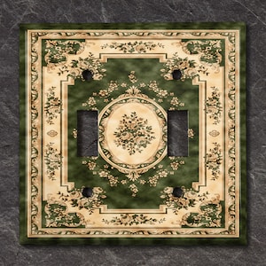 May include: A green and cream light switch cover with a floral pattern. The cover has a traditional design with a central oval surrounded by a square frame.