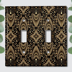 May include: A black light switch cover with a gold geometric pattern. The pattern features swirls and stylized flowers.