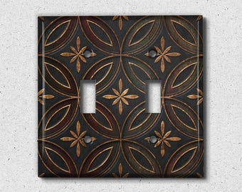 May include: A double light switch cover with a decorative design featuring a repeating pattern of overlapping circles and stylized flowers in shades of brown, gold, and black.