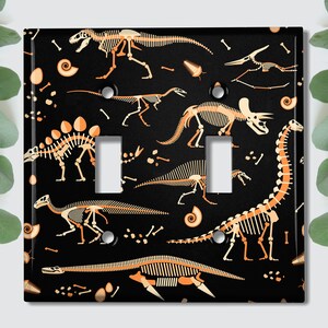 May include: Black light switch cover with a repeating pattern of orange dinosaur skeletons on a black background.
