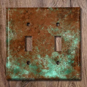 May include: A double light switch cover with a rustic, distressed copper and green patina finish. The cover has a textured surface and a weathered look.