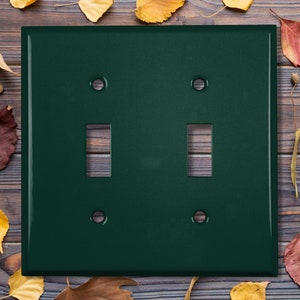 May include: A dark green double light switch plate with two toggle switches and two round screw covers.