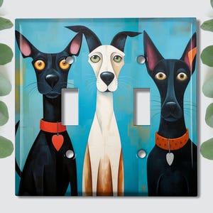 May include: A light blue background with three dogs. The dog on the left is black with red collar and a heart charm. The dog in the middle is white with black spots and a brown collar. The dog on the right is black with a brown collar and a silver charm. The dogs are looking at the viewer.