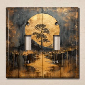 May include: A light switch cover with a dark background and a gold moon with a silhouette of a tree in the center. The moon is reflected in the water below.
