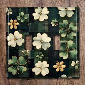 May include: A light switch cover with a green and white plaid background featuring a pattern of four-leaf clovers and white flowers with yellow centers.