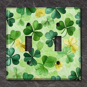 May include: A light green double light switch cover with a watercolor pattern of green shamrocks and yellow four-leaf clovers.