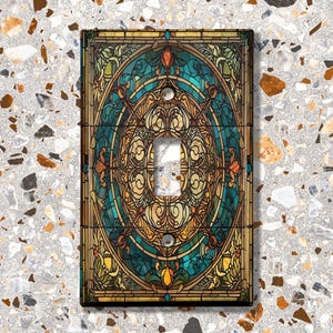 May include: A light switch cover with a stained glass design featuring a circular pattern in shades of blue, gold, and brown.
