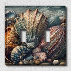 May include: A light switch cover featuring a close-up of a collection of seashells in various shades of brown, blue, and white. The shells are arranged in a cluster, with some overlapping and others partially visible. The background is a blurred image of a beach scene.