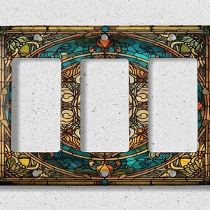 May include: A triple light switch cover with a stained glass design featuring a blue, green, and gold color scheme. The design is intricate and features floral and geometric patterns.