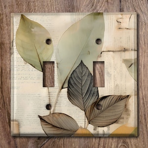 May include: A decorative light switch cover featuring a botanical design. The cover has a clear, glossy finish with a collage of leaves in shades of green, brown, and beige. The background includes handwritten script. The switch plate has three toggle switch openings.