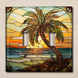 Peut inclure: Une plaque de prise de courant en verre teinté représentant un palmier sur une plage au coucher du soleil. Les couleurs sont vives et comprennent des nuances de bleu, de vert, de jaune, d'orange et de marron.