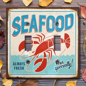 May include: A vintage-style light switch cover with a red lobster illustration and the text "Seafood, Always Fresh, Our Specialty!" The cover has a rustic, weathered look with a blue and white background.