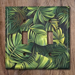 May include: A double light switch cover with a tropical leaf pattern. The cover features a green, yellow, and brown color scheme with a realistic painting style.