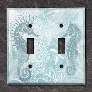 Peut inclure: Plaque d'interrupteur décorative avec un motif sur le thème de la mer. La plaque a un fond bleu clair avec des illustrations de coraux blancs et d'hippocampes. Elle comporte deux ouvertures d'interrupteur et quatre trous de vis.