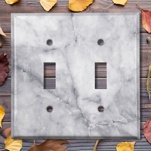 May include: A white marble light switch cover with two toggle switches. The cover has a light gray veining pattern.