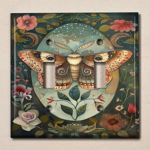 May include: A light switch cover with a whimsical design featuring a large, colorful moth with intricate wings against a backdrop of lush greenery and delicate flowers.