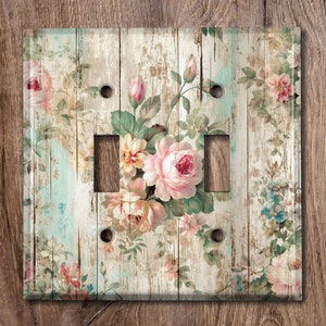 May include: A light switch cover with a floral design on a distressed wood background. The flowers are pink, white, and blue.
