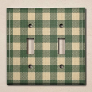May include: A green and cream gingham patterned light switch cover with two toggle switches.
