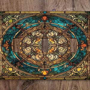 May include: A stained glass light switch cover with a circular design featuring blue, green, yellow, and brown colors. The design is intricate and features a variety of geometric shapes.