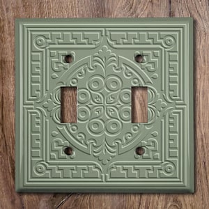 May include: A light green double light switch cover with an embossed geometric design.