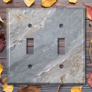 May include: A double light switch cover with a gray and brown marble pattern. The cover is made of slate and has a modern design.