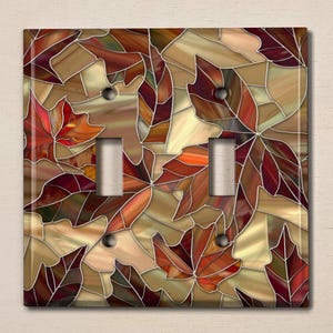 May include: A decorative light switch cover featuring a stained glass design of autumn leaves in shades of red, orange, brown, and gold.
