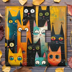 May include: A light switch cover featuring a colorful illustration of a group of cats with various expressions. The cats are depicted in a playful and whimsical style, with bright colors and bold lines. The background is a yellow-orange color with a textured look.