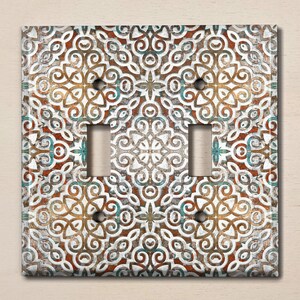 May include: A double light switch cover with a decorative design featuring a white background with brown, blue, and red intricate patterns.