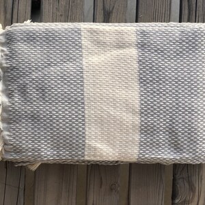 May include: A gray and white striped throw blanket with fringe on the edges. The blanket is made of a soft, textured fabric.