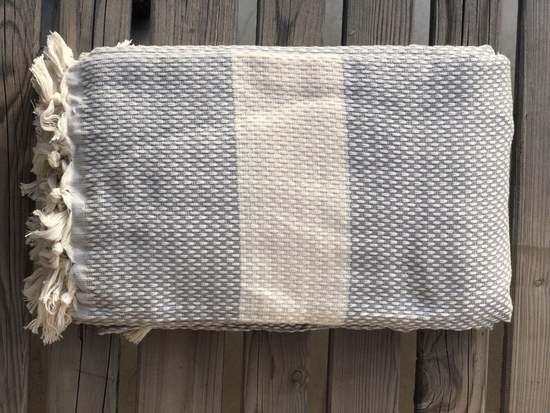 May include: A gray and white striped throw blanket with fringe on the edges. The blanket is made of a soft, textured fabric.