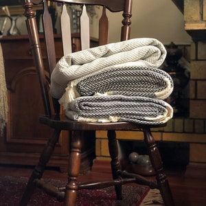 May include: A wooden chair with a woven throw blanket folded on top. The chair has a dark brown finish and a spindle back. The blanket is white and black with a geometric pattern.