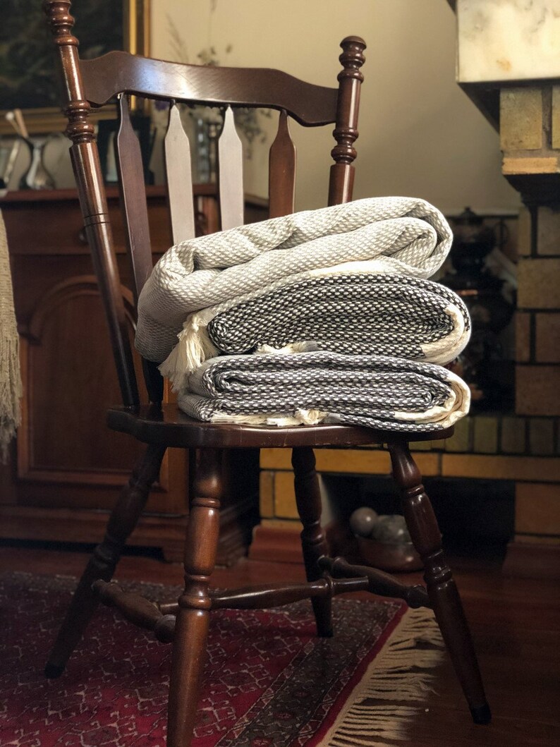 May include: A wooden chair with a woven throw blanket folded on top. The chair has a dark brown finish and a spindle back. The blanket is white and black with a geometric pattern.