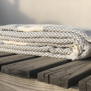 May include: A gray and white waffle weave Turkish towel with fringe. The towel is folded and placed on a wooden surface.
