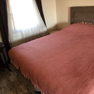 May include: A bedroom with a large bed with a pink and white chevron patterned duvet cover. The bed has a brown headboard and a white nightstand. The room has a window with white curtains and brown drapes.