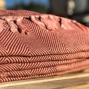 May include: A folded pink and brown throw blanket with fringe tassels. The blanket has a chevron pattern.