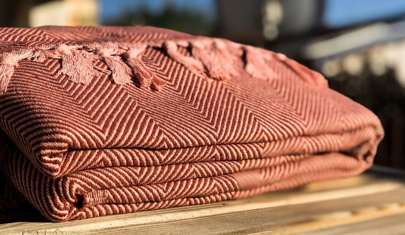May include: A folded pink and brown throw blanket with fringe tassels. The blanket has a chevron pattern.