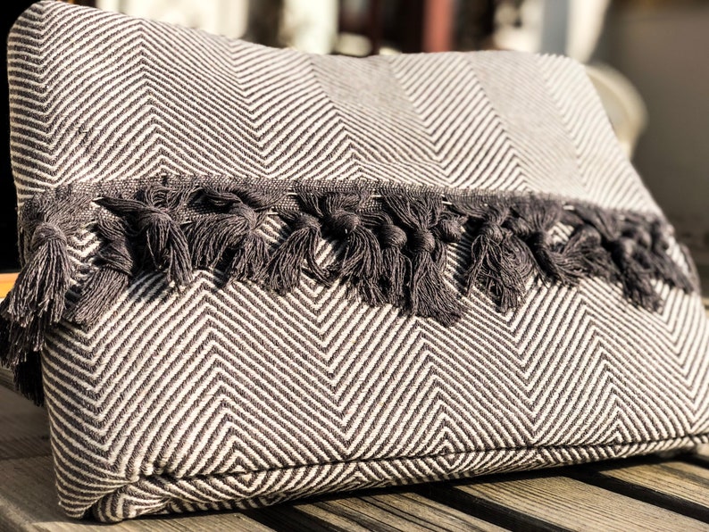 May include: A black and white chevron patterned throw pillow with a black tassel trim.
