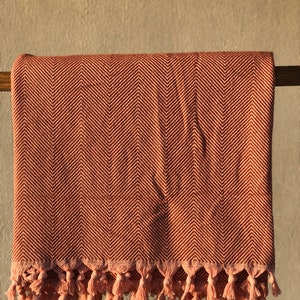 May include: A pink and brown herringbone throw blanket with a fringe border. The blanket is draped over a wooden rod.